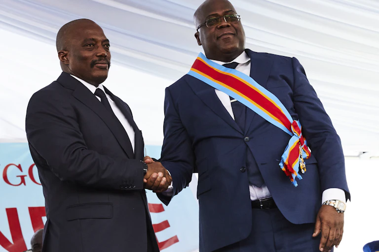 Former DRC President Joseph Kabila, left, shakes hands with his successor Felix Tshisekedi at his inauguration. Both men are wearing navy-blue suits.