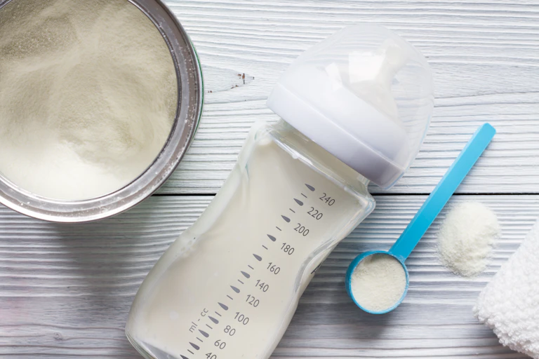 A baby bottle lays on a table next to a can of infant formula.