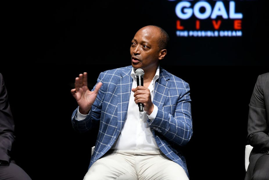 Patrice Motsepe, seated,speaks into a microphone and gestures 