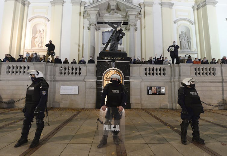 Members of a far-right organization stand guard in front of the Holy Cross Church, fronted by a row of police officers, in Warsaw on Oct. 28, 2020