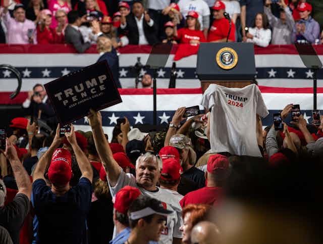 A Trump supporter holds up a t-shirt with 'Trump 2024' printed on it.