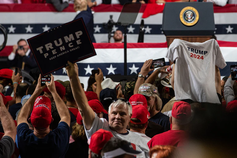A Trump supporter holds up a t-shirt with 'Trump 2024' printed on it.