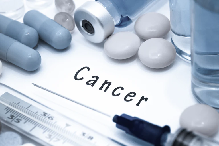 Medicinas y una jeringuilla junto al texto 'cáncer' escrito en el fondo blanco.