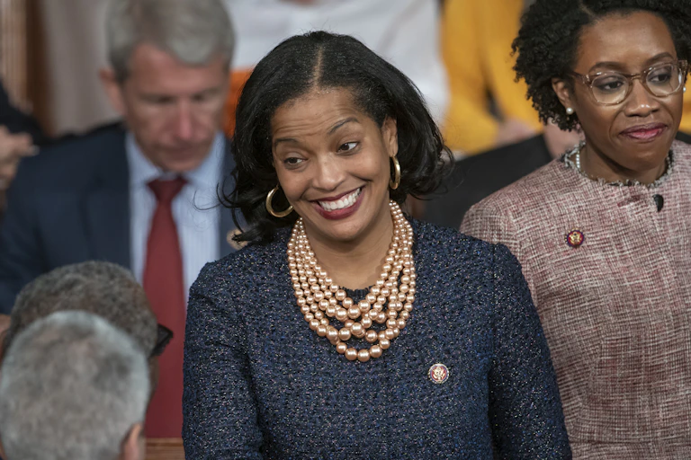 A woman in pearls and a dark suit jacket smiles at an audience