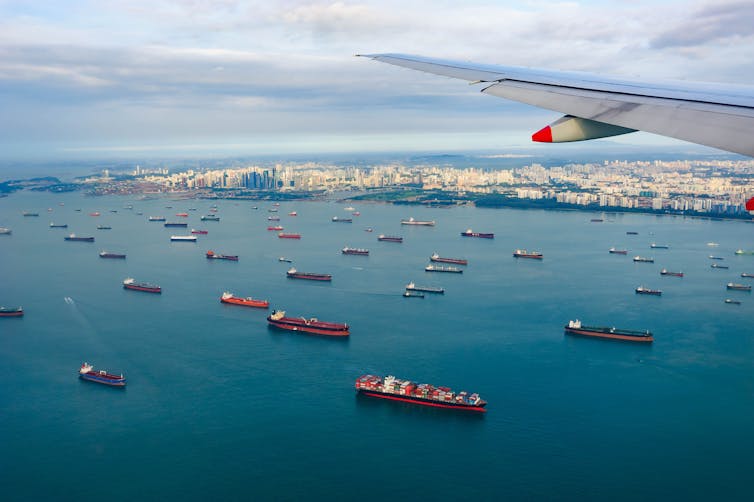 Cargo ships waiting offshore with plane wing in foreground