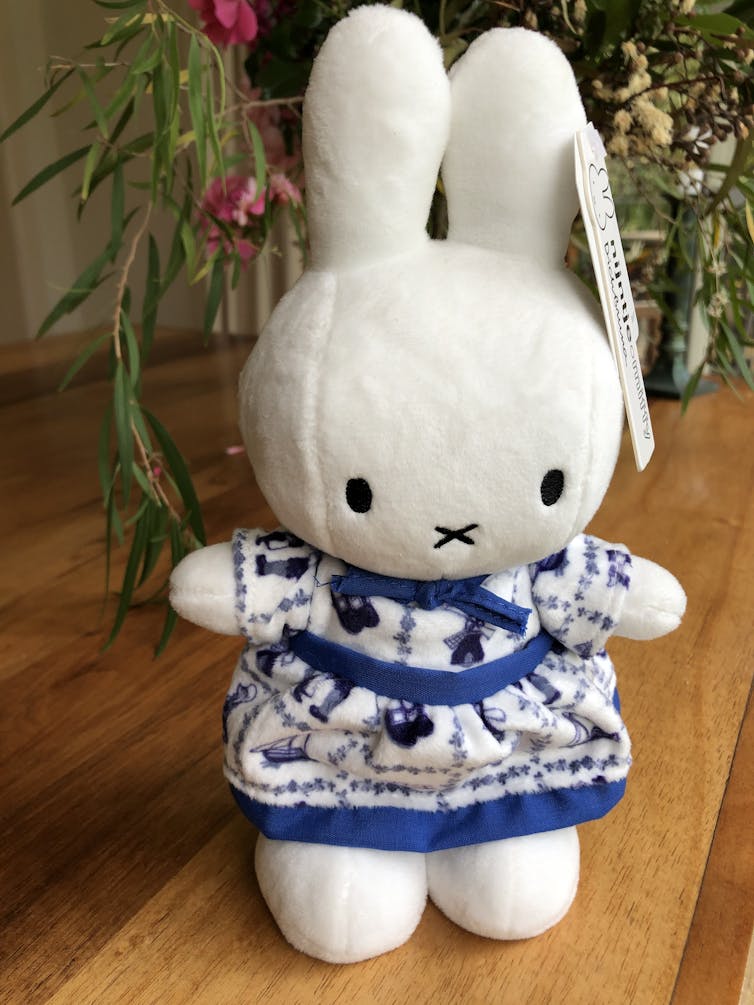 A bunny soft toy in blue and white dress.