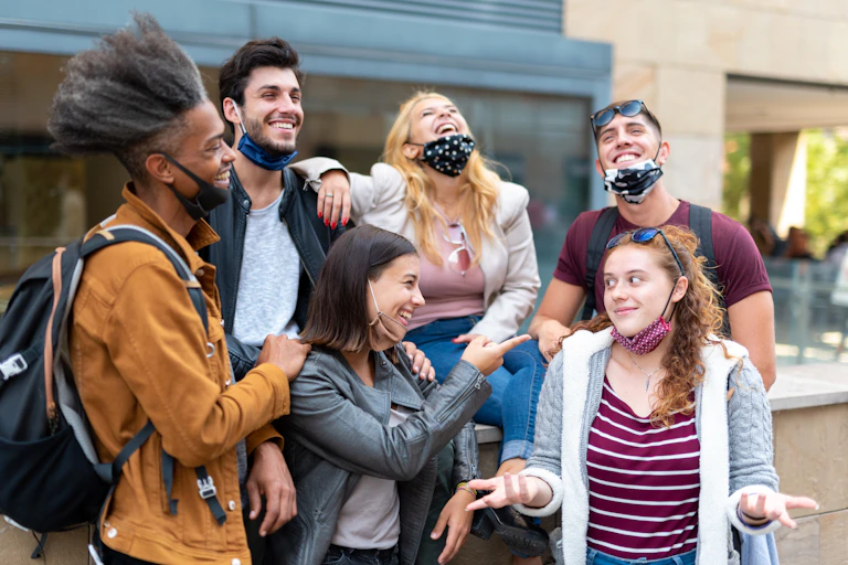 Group of young people stood close talking with masks worn on their chins.