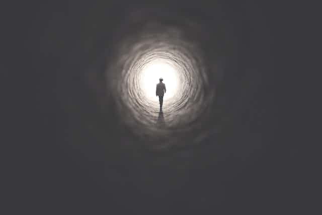 An illustration of a man in a suit and hat walking towards the light at the end of a tunnel.