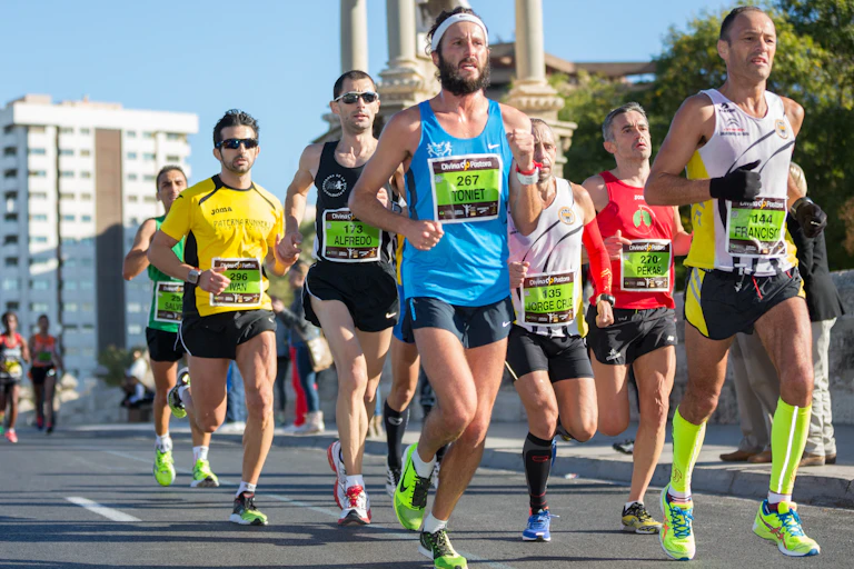 A group of male marathon runners running in a pack on an empty city road.