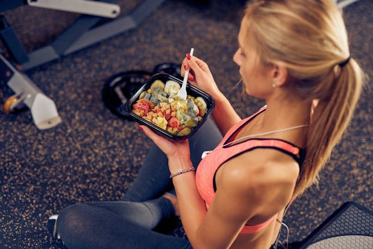 Woman sitting on the floor of the gym eating a healthy meal.