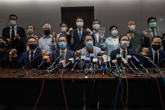 Group of Hong Kong opposition MPs wearing masks and holding hands, in front of microphones