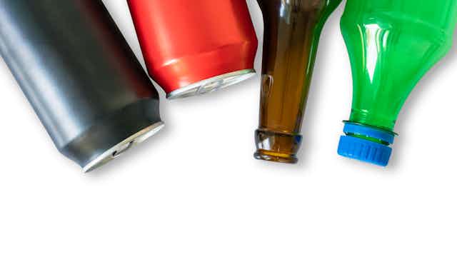 Two aluminium cans, a brown glass bottle and a green plastic bottle on a white background.