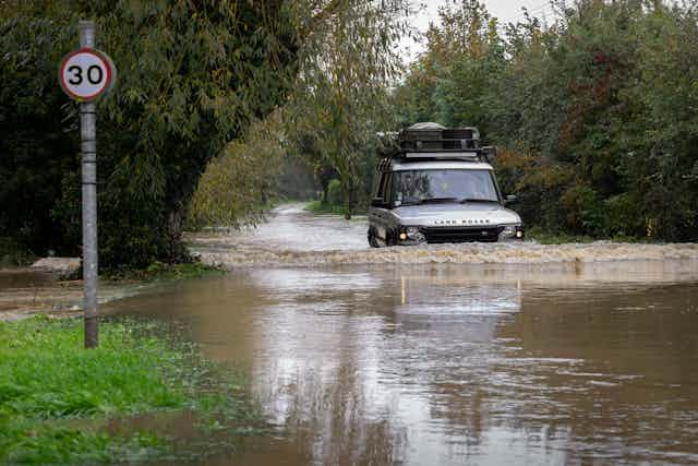 A Land Rover car drives along a flooded street.