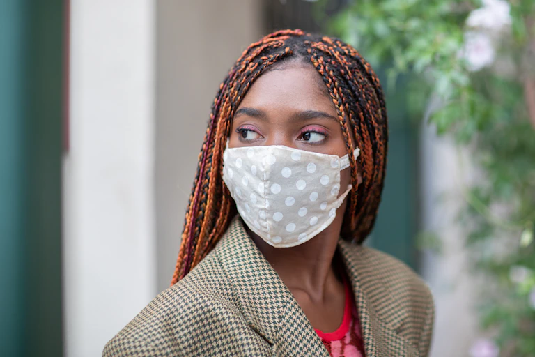 Una chica joven con mascarilla higiénica reutilizable de lunares blancos sobre fondo gris
