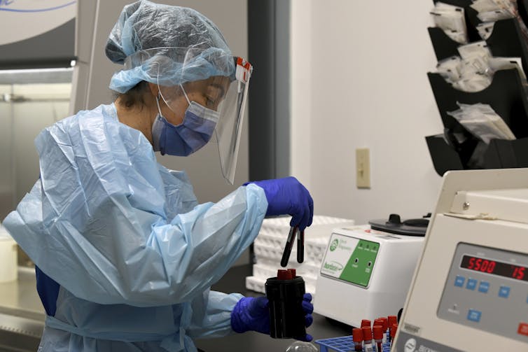 A researcher wearing PPE working with blood samples for vaccine development