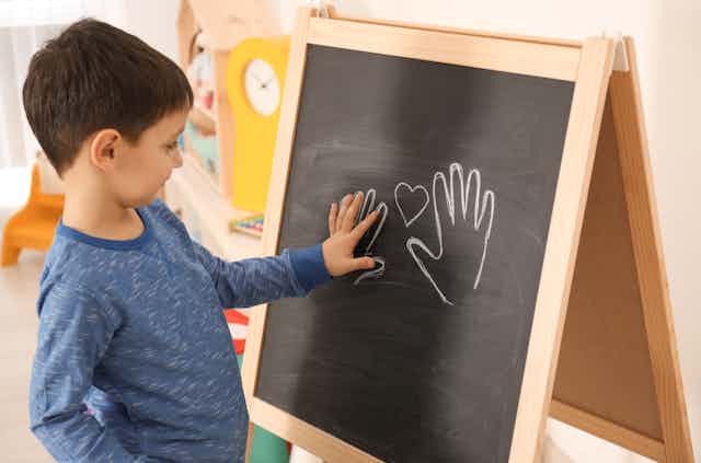 A young boy traces his hand on a blackboard.