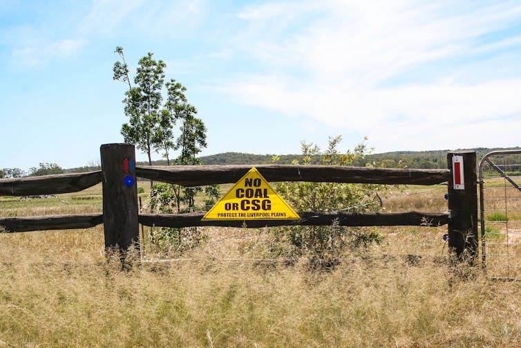 A yellow triangle sign that says 'no coal or coal seam gas' on a wooden fence.