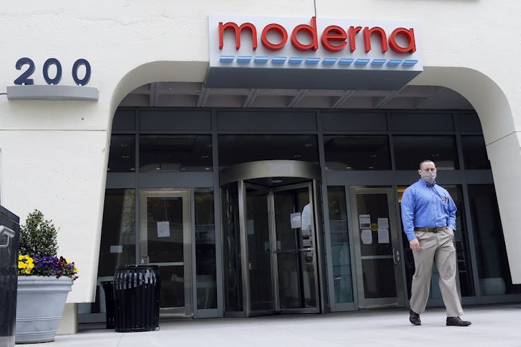 A man in a face mask walks past the entrance to a white building, under the name Moderna in red letters.