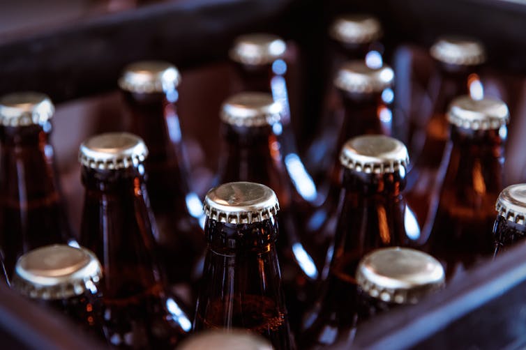 A crate full of brown bottles with silver caps.