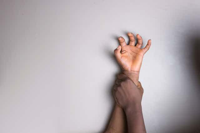 Una mano de hombre aprisiona contra una pared el brazo de una adolescente.