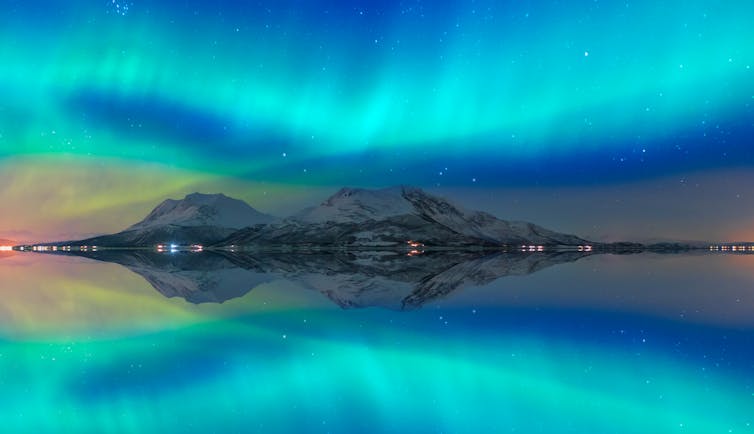 A band of turquoise light in the sky is reflected in the Norwegian fjord below.