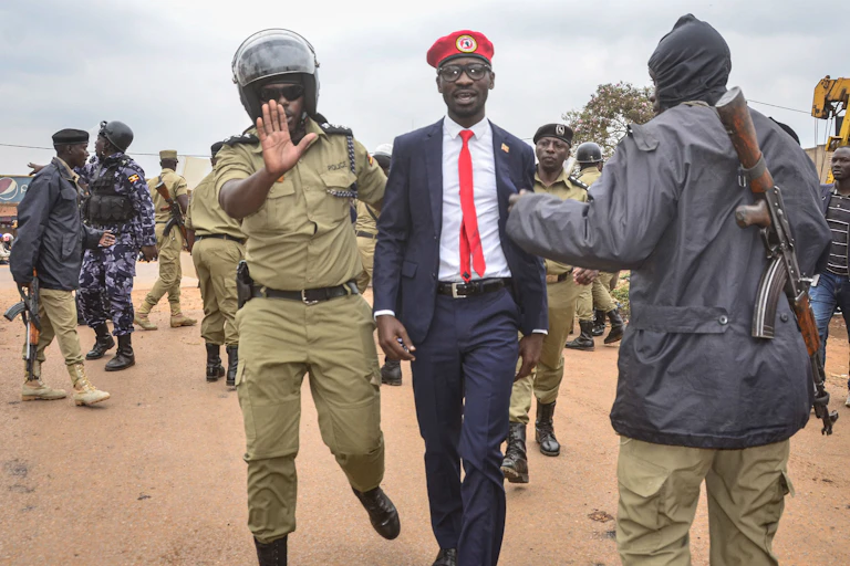 Ugandan singer-turned-politician Robert Kyagulanyi aka Bobi Wine (C) is escorted by a police officer as he is arrested on charges of unlawful assembly before starting his first public meeting ahead of presidential election next year on January 6, 2020, in Kasangati town, suburb of Kampala. - Wine, a popular figure among young Ugandans, announced last year he would challenge the incumbent President in the 2021 elections, and on January 6 was scheduled to begin a week-long series of consultations ahead of the vote.