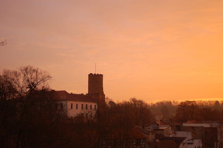 A small castle with a single turret sits amid trees at dusk.