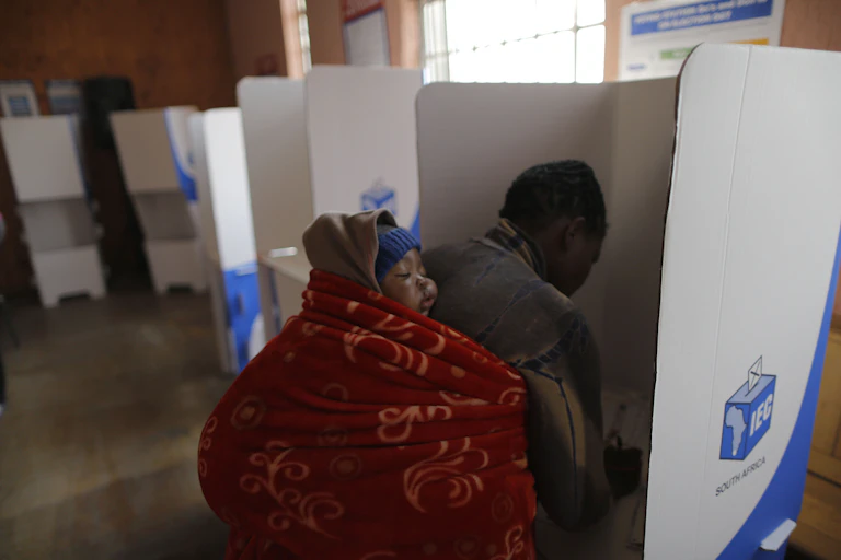 A woman carrying a baby on her back makes her mark at a polling booth