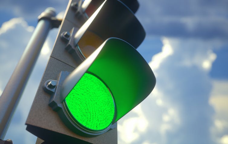 Green traffic light against backdrop of cloudy sky