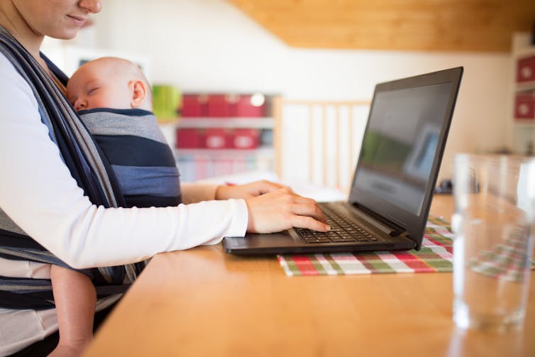 A woman works while holding a baby.