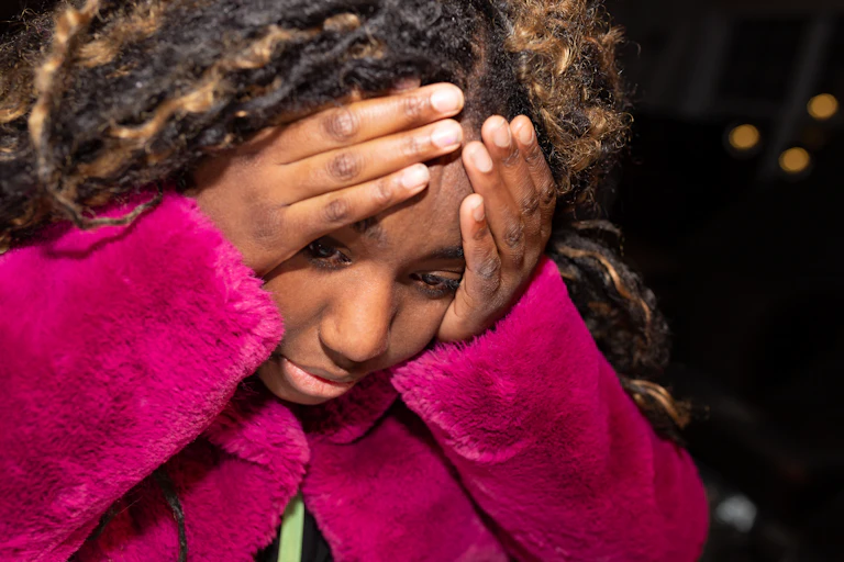 Teenage girl looks down while holding her head in her hands
