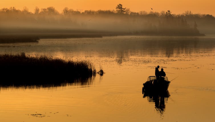Men fish from a boat as the sun rises.