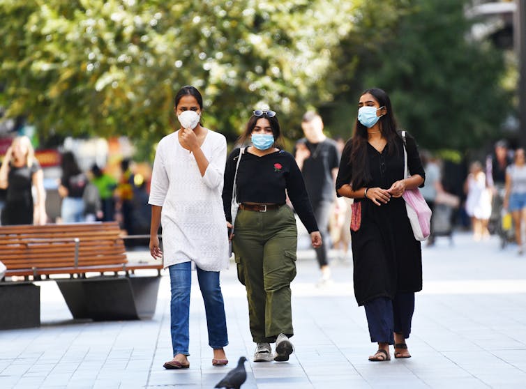 Three women walk through Rundle Mall wearing masks.