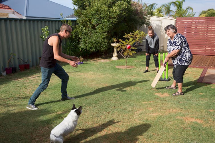 A family play cricket in the back yard