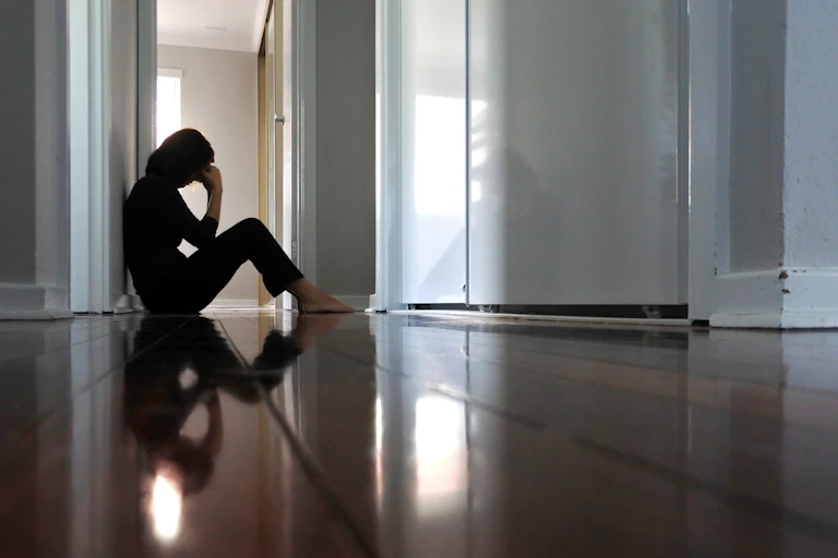 Woman sitting on the floor at home, appears depressed.
