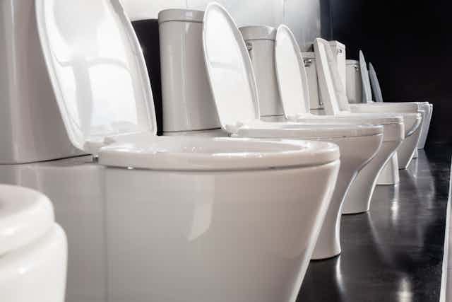 Row of white ceramic toilet bowls on black wall.