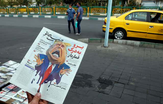Man holding Iranian newspaper with caricature of Donald Trump on front page.