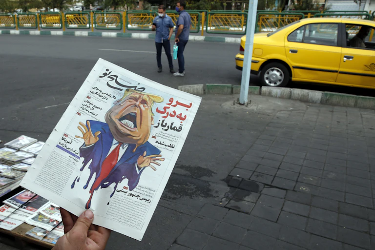 Man holding Iranian newspaper with caricature of Donald Trump on front page.