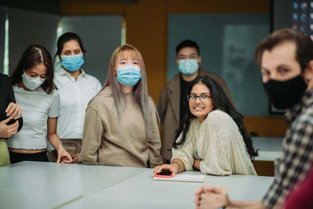 A group of Asian American students mostly wearing masks sit in class.