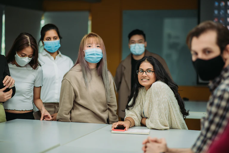 A group of Asian American students mostly wearing masks sit in class.