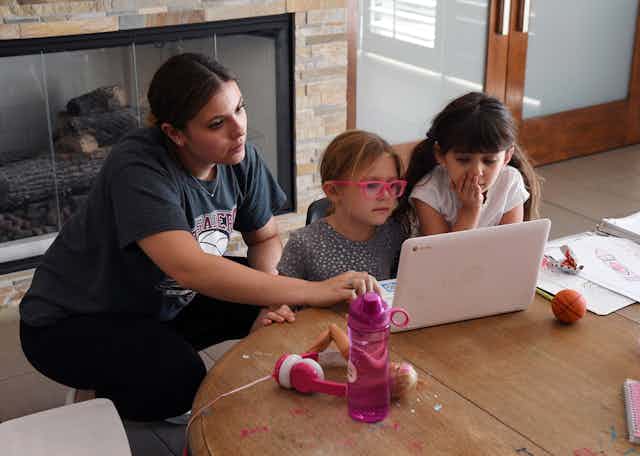 A woman and two young girls work together on a laptop