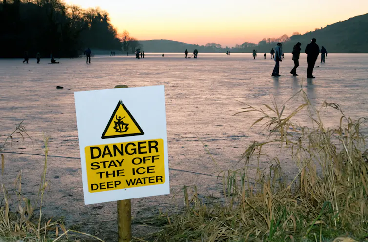 people walking on a frozen lake with a danger 'thin ice' sign in the foreground