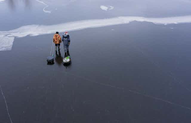 two men pulling sleds across a frozen lake after fishing