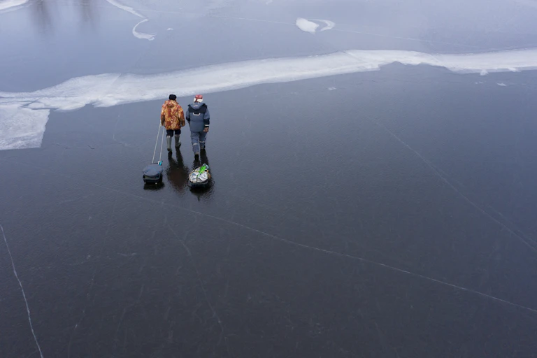 two men pulling sleds across a frozen lake after fishing