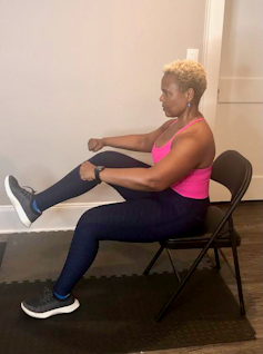 A woman sits in a folding chair, lifting one knee up.