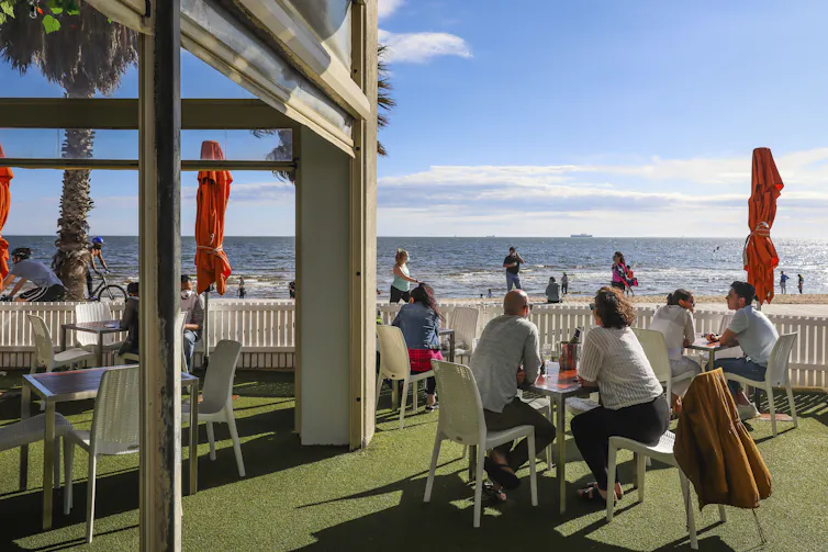 Diners sit on a restaurant patio overlooking a beach.