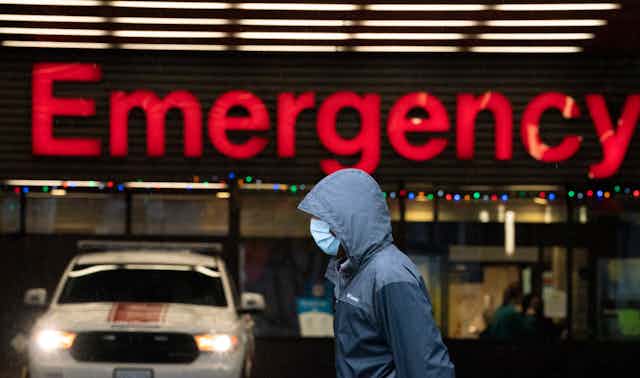 A person wearing a mask walks past a large red emergency sign.
