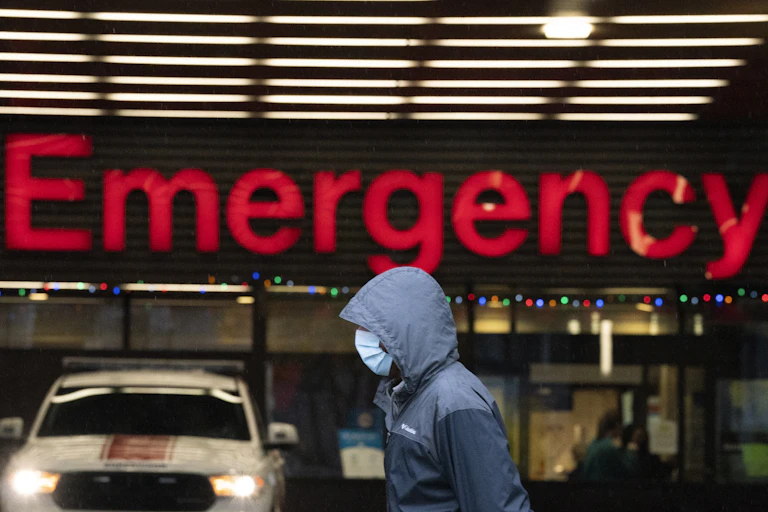 A person wearing a mask walks past a large red emergency sign.