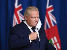 Doug Ford removes his face mask at a news conference.