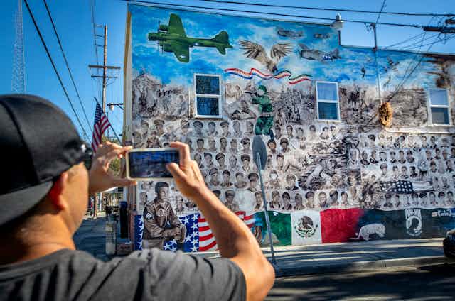 Man uses cell phone to photograph a mural with Mexican and American flags